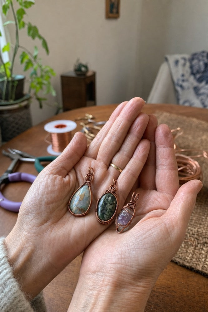 Three finished copper wire-wrapped pendants resting in a pair of hands